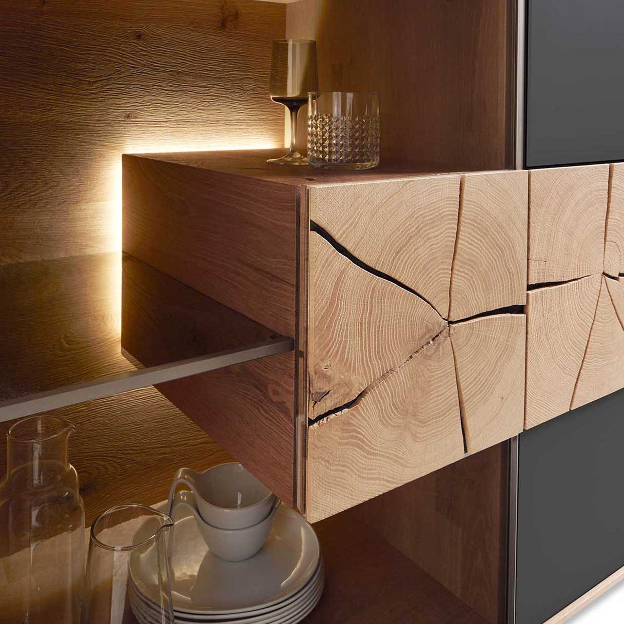 Detailbild eines beleuchteten Hirnholzblocks aus massiver Kerneiche Umato mit sichtbarer Holzmaserung und charakteristischen Holzrissen an Glastür eines CAYA Sideboards oder einer Hängevitrine. 