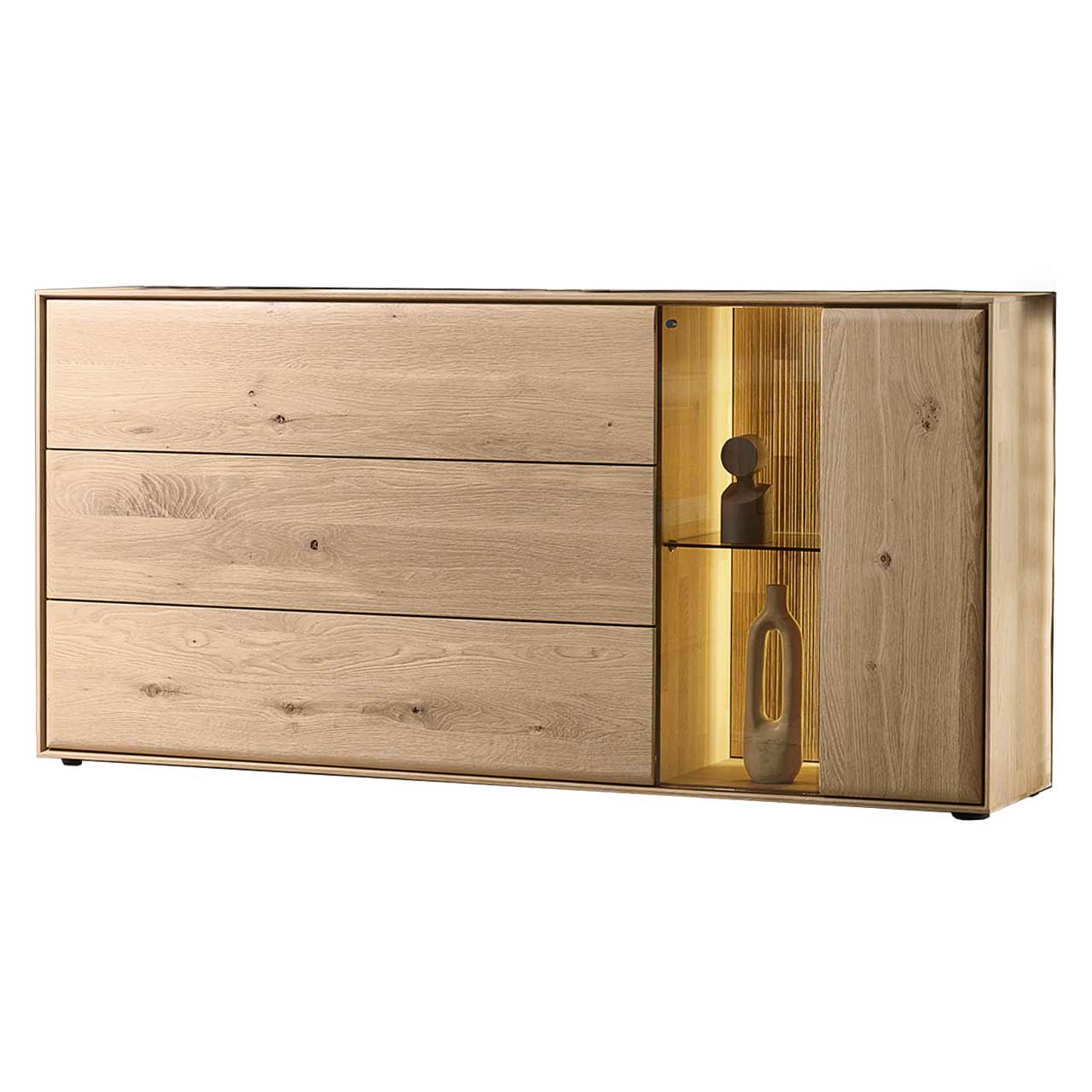 Modernes Sideboard aus massiver Kerneiche Natur mit einer beleuchteten Glas/Holztür rechts und einer Holzklappe und zwei Holzschubkästen links - in Seitenansicht. 