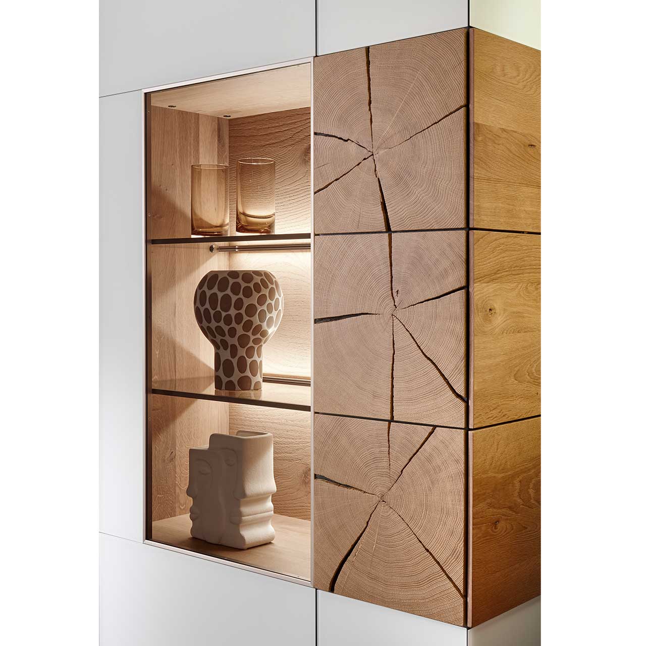 Detailaufnahme des CAYA Highboards Nr. 7170-7083W mit links einer Glastür mit drei beleuchteten Böden links und einer Holztür mit drei vertikal verlaufenden Hirnholzscheiben rechts.