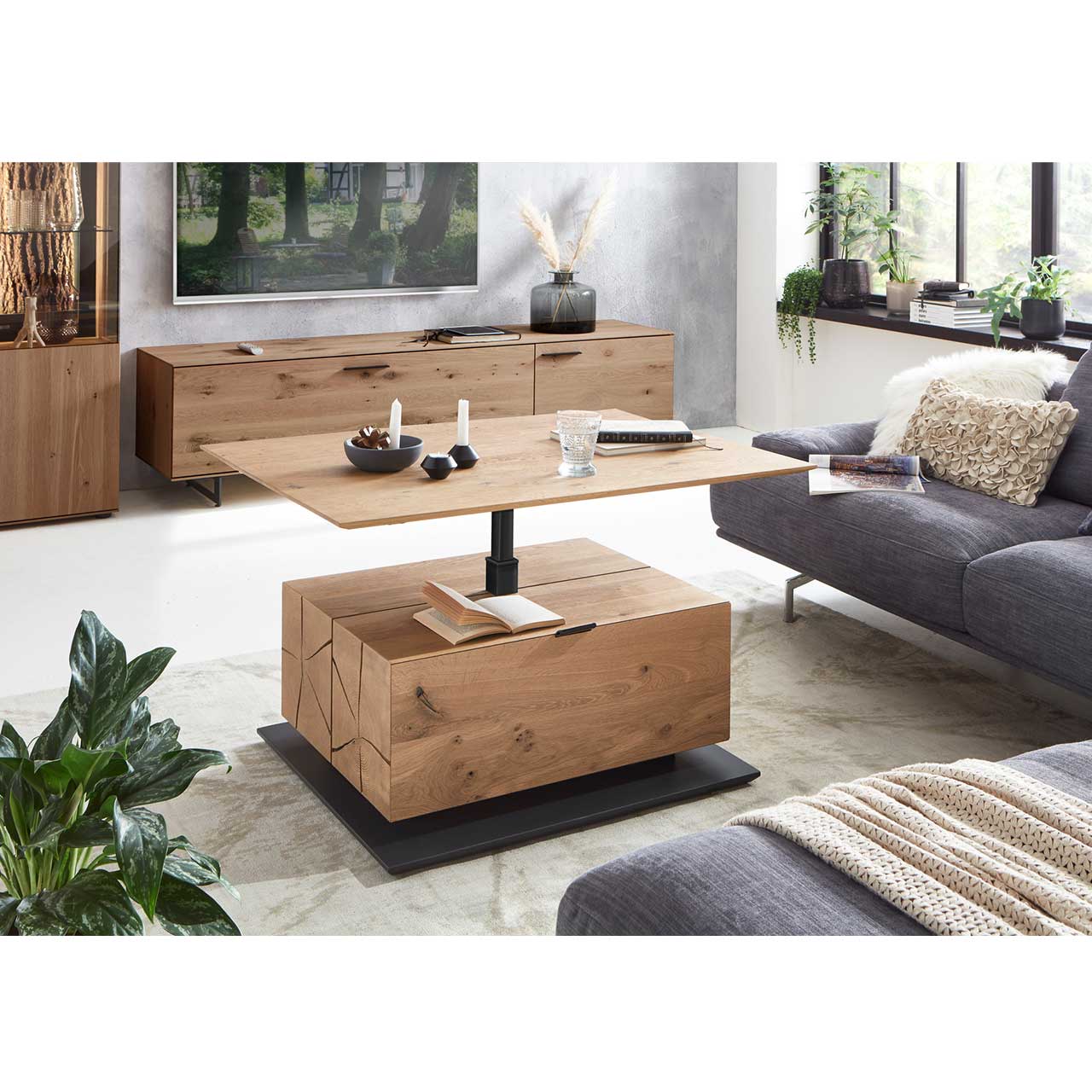 Moderner Couchtisch mit hochgefahrener Tischplatte, Hirnholzblock aus massiver Kerneiche, Klappe und Stauraumfach auf dunkler Bodenplatte – im Wohnzimmer stehend.