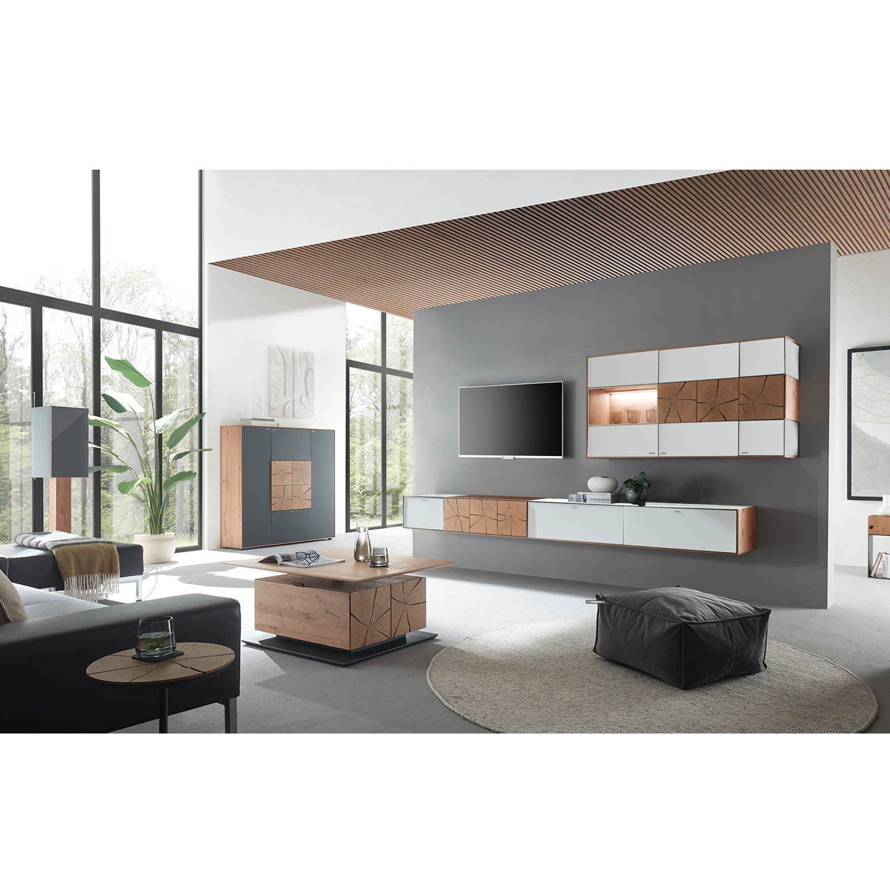 Wohnzimmer mit TV und moderner Wohnwand aus massiver Kerneiche und Mattglas weiß Fronten, mit schmalem Hängelowboard und beleuchteter Hängevitrine. Links das passende Highboard. Im Vordergrund ein rechteckiger Holz-Couchtisch.