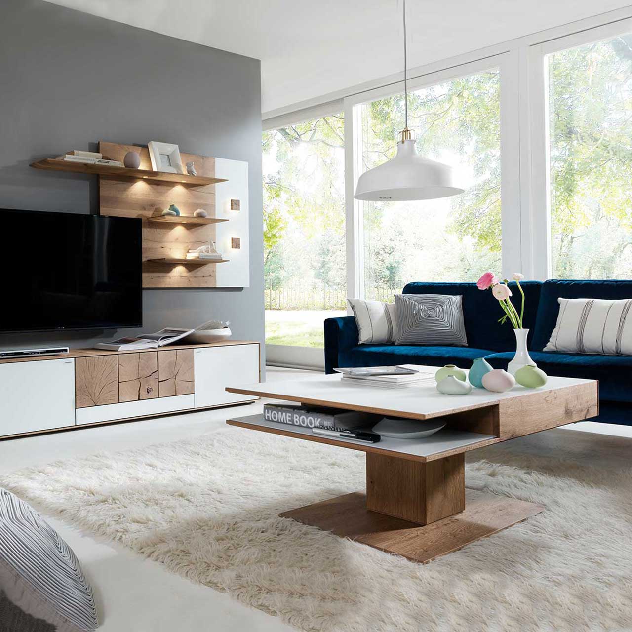 Wohnzimmer mit moderner Massivholz Wohnwand aus Kerneiche Umato mit Mattglas weiß Fronten: Lowboard mit dekorativen Hirnholzscheiben, beleuchtetes Wandpaneel mit Ablageböden, davor passender, rechteckiger Holz-Couchtisch mit sichtbarem Ablagefach.